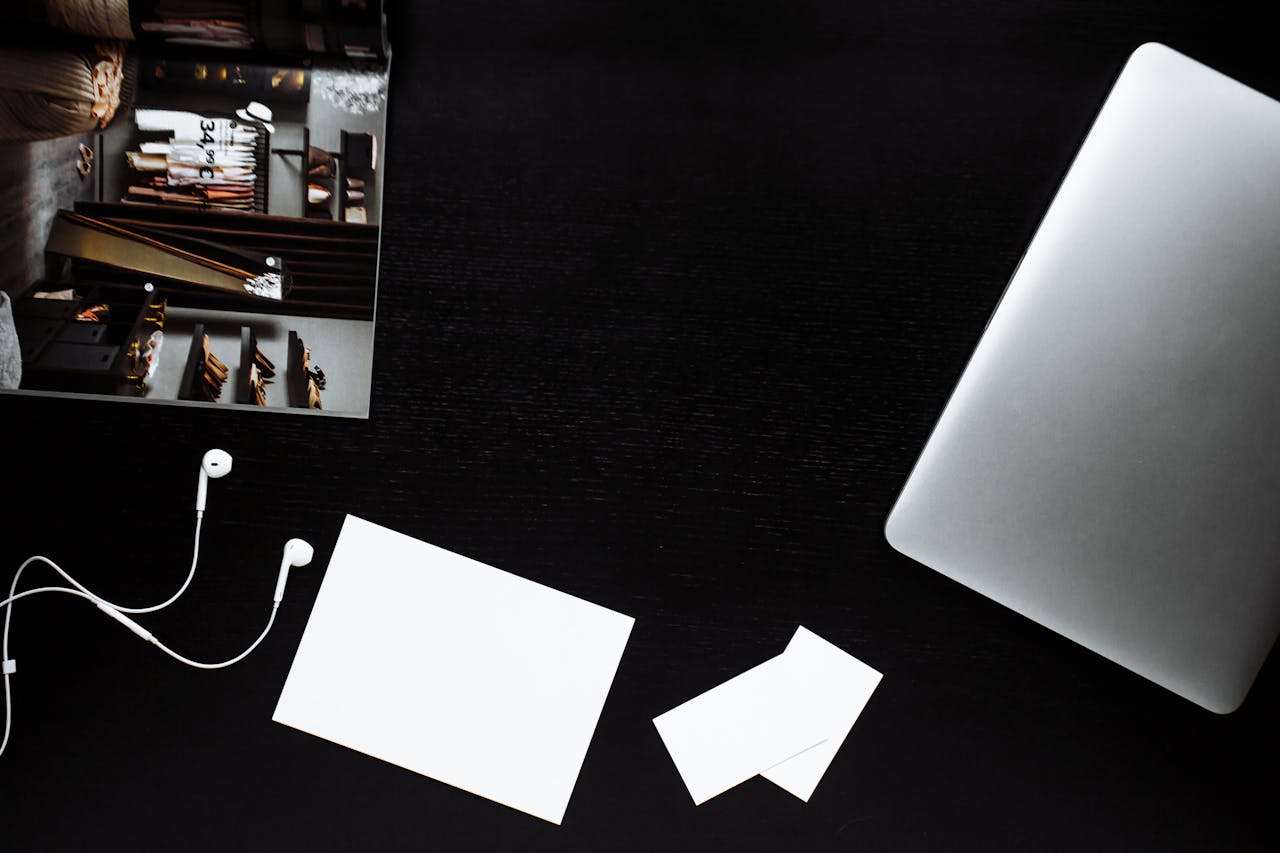 Minimalist flatlay with laptop, earphones, and stationery on a sleek black desk.